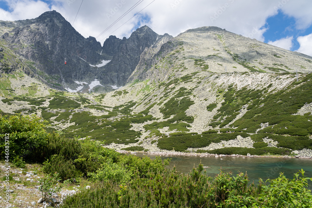 Scenic view of Skalnate Pleso (Rocky Tarn) and cable car heading to Lomnicky Stit peak in High Tatra mountains, Slovakia. Beautiful clean nature in Central Europe, cloudy day in summer