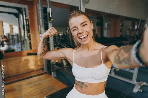 Panel kuchenny z motywem Close up young sporty athletic sportswoman woman in white sportswear warm up training sit near treadmill trainers do selfie shot on mobile cell phone show biceps in gym indoors Workout sport concept