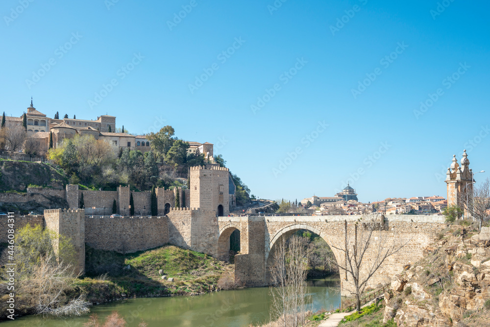 Old bridge of San Martín and in the background the monumental city of Toledo. Beneath the arches of the bridge the river Tagus passes placidly.