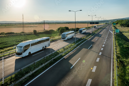 Series of modern White buses traveling on a wide highway in a rural backdrop. Convoy of buses. Highway transportation of passengers in a bus line.