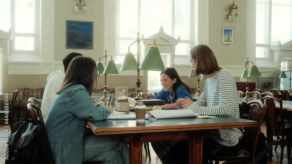 A group of young students are sitting at the desk and talking in the library hall