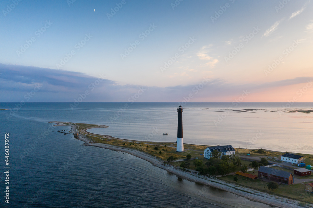 Aerial view over sunset colored seascape with the beautiful clouds and rising moon over long spit  with the historic lighthouse and visitor center in Sõrve Säär, Saaremaa isl., Estonia