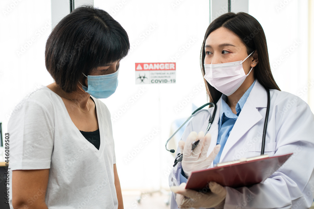 Asian doctor standing in front Quarantine room of and explaining patient relatives About symptoms And how to treat disease Coronavirus (COVID-19). Treatment, preventive measures, and vaccines concept Asian doctor standing in front Quarantine room of and explaining patient relatives About symptoms And how to treat disease Coronavirus (COVID-19). Treatment, preventive measures, and vaccines concept