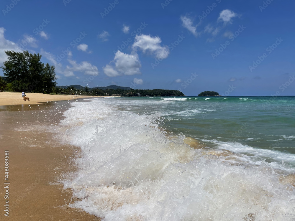 Sea, waves, water splash, splashes in the air. Deserted beach. Woman walks with a dog, walk on the sand along the sea line. Green hill on the horizon. Small island on a distance. Seascape. Thailand 