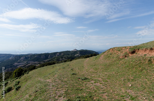 imagen de la cima de una montaña con vistas a otra montaña con el cielo azul y con nubes 