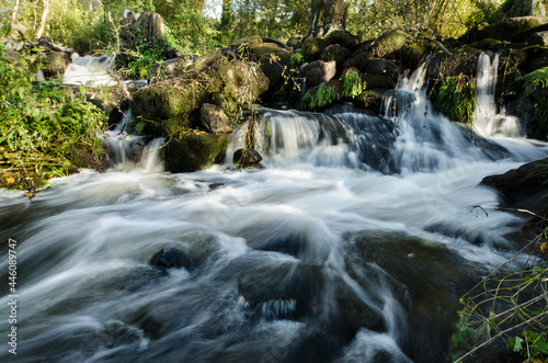 imagen de larga exposición con efecto seda en el río entre las piedras y con los árboles de fondo