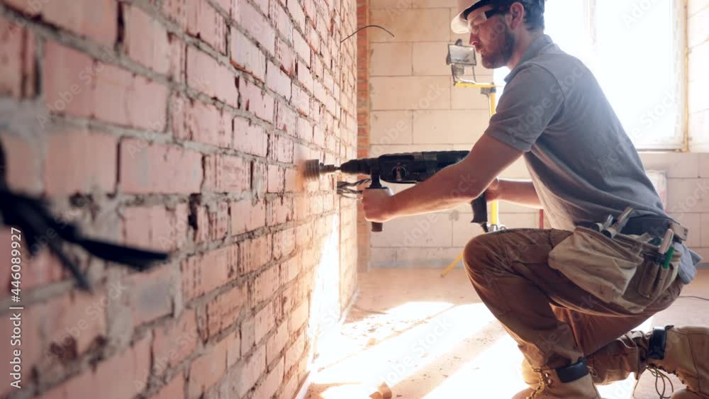 The builder is drilling a wall, he will be drilling walls, construction concept, laying of electricity. The builder is drilling a wall, he will be drilling walls, construction concept, laying of electricity.