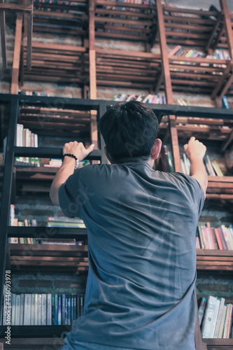 Young man climbing ladder for searching some book at bookshelf , wisdom , learn and education concept