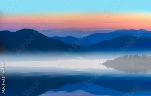 Beautiful landscape with high blue mountains with illuminated peaks, and mountain lake reflection