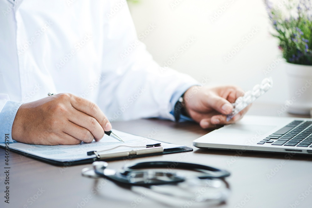 Male physician medicine doctor or pharmacist sitting at the worktable, holding pills in hand and writing the prescription. Medical care, pharmacy. Male physician medicine doctor or pharmacist sitting at the worktable, holding pills in hand and writing the prescription. Medical care, pharmacy.