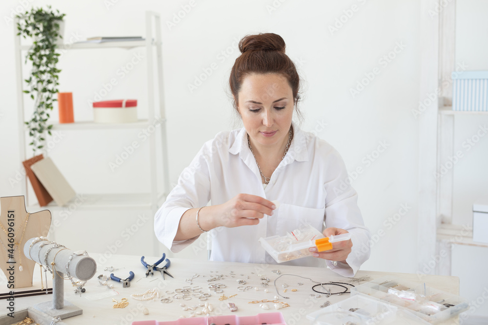 Charming young enthusiastic caucasian woman making beautiful unique costume jewelry while sitting at her desk. Concept of hobby and pleasant work Charming young enthusiastic caucasian woman making beautiful unique costume jewelry while sitting at her desk. Concept of hobby and pleasant work