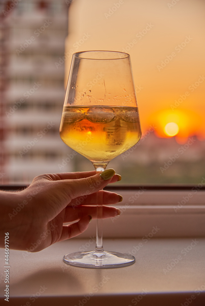 A woman's hand with a glass of wine on the background of a bright sunset.