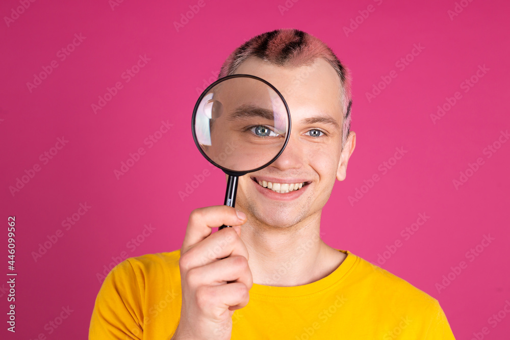 European handsome young man in yellow t shirt on pink background playful with magnifier, bright portrait, pink hair European handsome young man in yellow t shirt on pink background playful with magnifier, bright portrait, pink hair