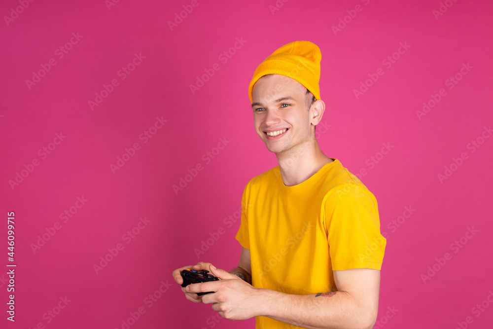 European handsome young man in yellow t shirt on pink background gamer with joystick playing games happy smiling cheerful European handsome young man in yellow t shirt on pink background gamer with joystick playing games happy smiling cheerful