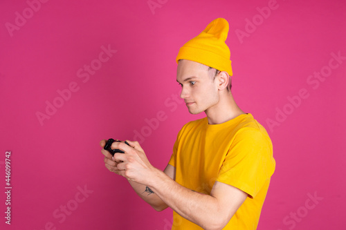 European handsome young man in yellow t shirt on pink background gamer with joystick playing games