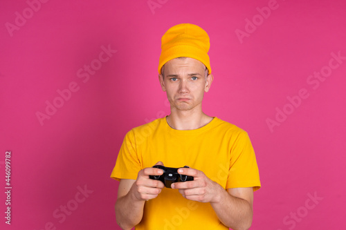 European handsome young man in yellow t shirt on pink background gamer with joystick unhappy disappointed sad