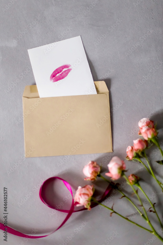 Envelope, lips print, ribbon and roses on a gray background