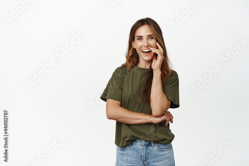 Image of beautiful adlult woman, middle aged ambitious female laughing, smiling with perfect white teeth, touch her face and look happy at camera, white background
