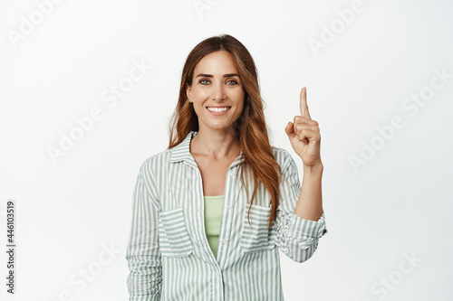 Image of confident, ambitious smiling woman, pointing finger up and looking determined, showing logo banner, advertisement store, standing against white background