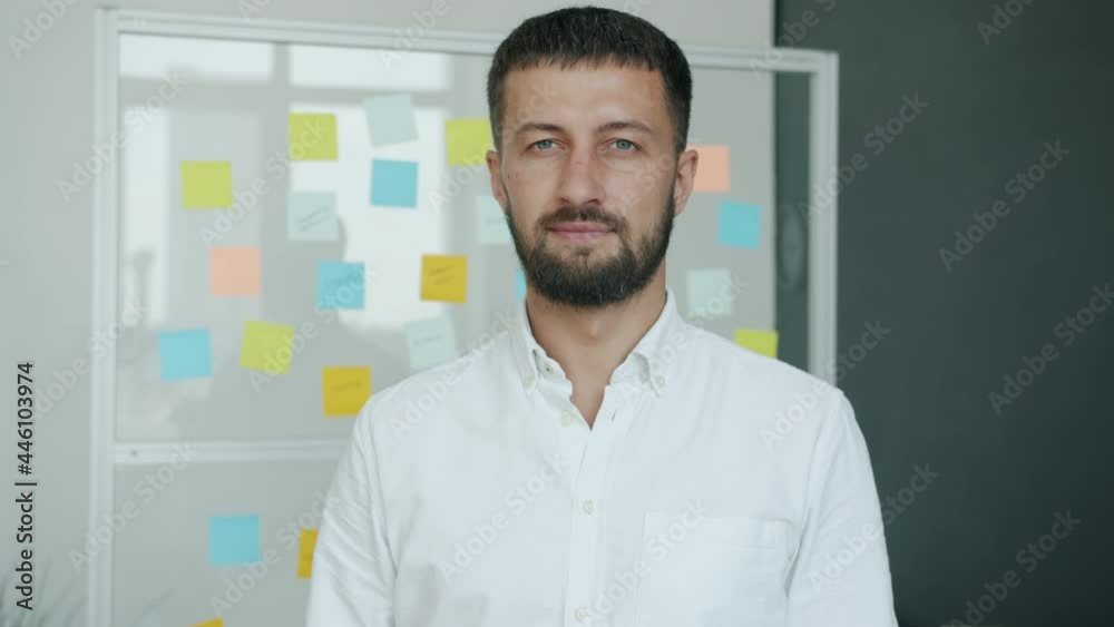 Slow motion portrait of handsome young businessman standing in creative office alone and looking at camera with serious face. Business and people concept. Slow motion portrait of handsome young businessman standing in creative office alone and looking at camera with serious face. Business and people concept.