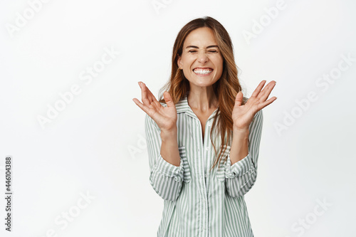 Happiness and wellbeing. Happy adult woman rejoicing, jumping from joy, close eyes and smiling broadly, winning, tirumphing over success, white background