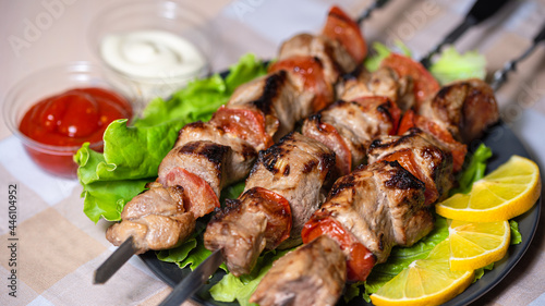 Pork shashlik with salad and lemon wedges on a black plate. Grilled meat on skewers with sauce.