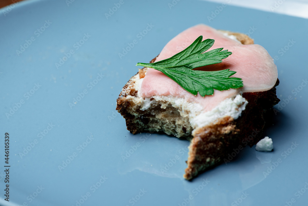 Bitten sandwich with cheese and ham on a blue plate. Bitten sandwich with cheese and ham on a blue plate.
