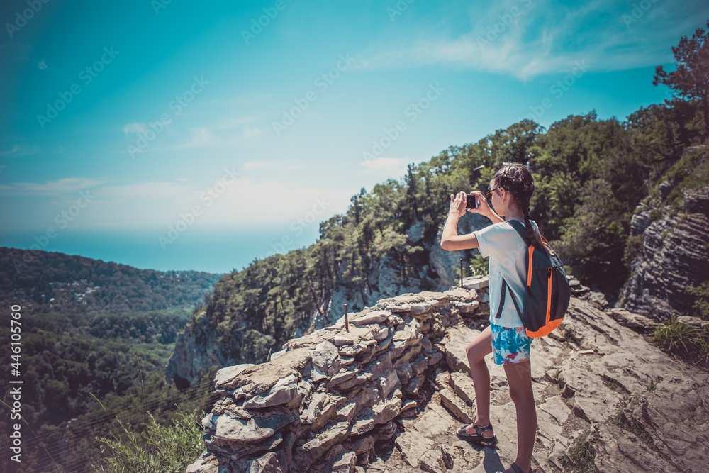 Naklejka premium A young girl holds a smartphone to take pictures of a beautiful mountain landscape