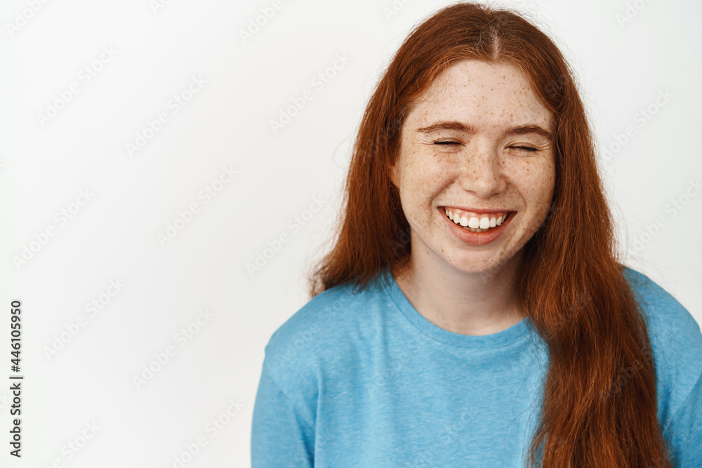 Positive people. Young happy girl with ginger long hair, laughing carefree with closed eyes, standing in blue tshirt against white background Positive people. Young happy girl with ginger long hair, laughing carefree with closed eyes, standing in blue tshirt against white background