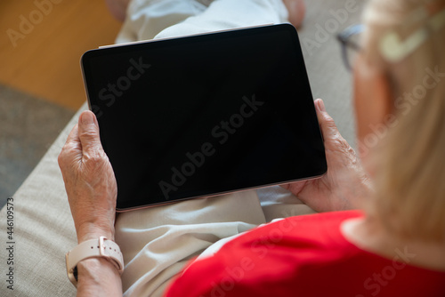 Senior woman holding blank screen tablet. Over the shoulder view.