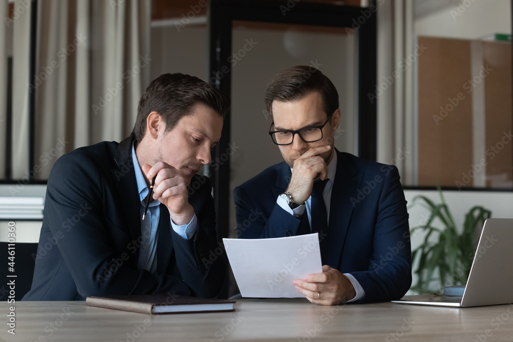 Two serious businessmen, focused business partners, coworkers reading document together. Legal expert, lawyer reviewing, studying contract, agreement text, giving consultation to client Two serious businessmen, focused business partners, coworkers reading document together. Legal expert, lawyer reviewing, studying contract, agreement text, giving consultation to client