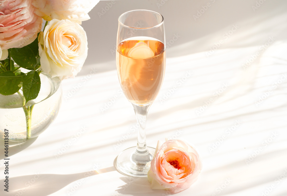 A glass of semi-sweet pink wine Pinot rose . Next to a bouquet of antique terry roses Pierre de Ronsard, Eden roses. Striped shadows on a white background. High quality photo