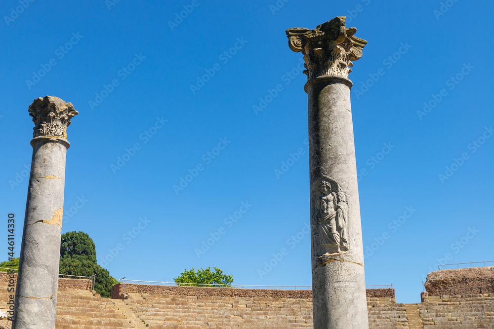 Panorama of the excavations of Ostia Antica, Rome Italy. Detail of the decorated columns in the theater of the archaeological park of Ostia with the steps of the imperial era, in summer with sky. 