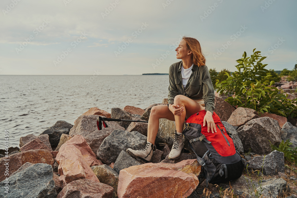 Pleased traveller resting on rocks with her backpack