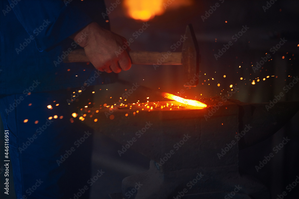 Fototapeta premium Experienced blacksmith manually forging molten metal with hammer on anvil. Close up of string male hands. Forge workshop. 