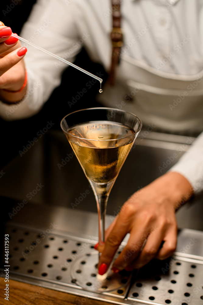 glass with drink in which female bartender adds drop of ingredient