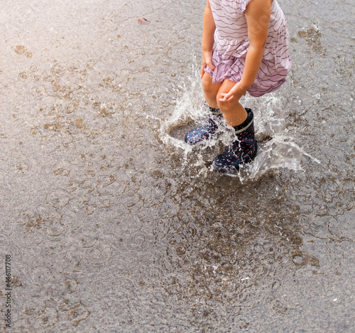 Child in rubber boots hops puddle in summer. Summer rain. Kind in Gummistiefeln hüpft Pfütze im Sommer. Sommerregen.