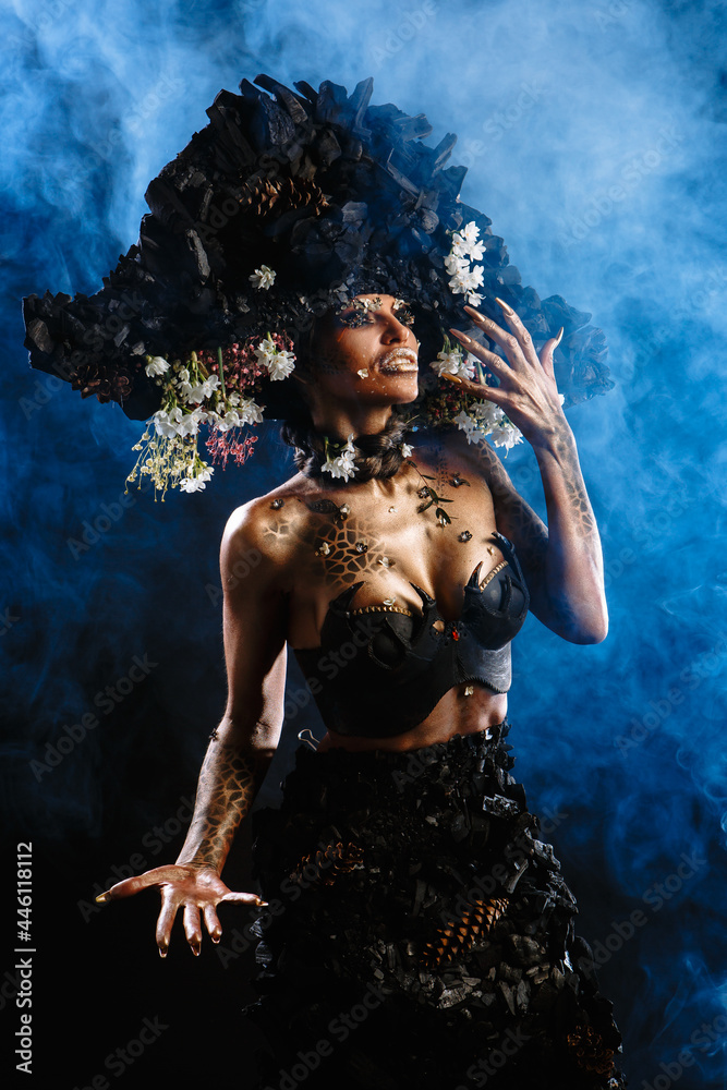 Portrait of a model in a headdress and dress made of coal. There is blue smoke behind the model