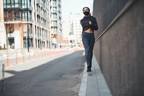 Pleased runner with cornrows jogging along the city street © Viacheslav Yakobchuk
