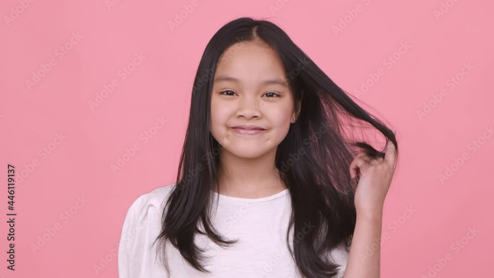 Little coquette. Cute playful asian girl playing with hair and smiling to camera, flirting and smiling, pink background Little coquette. Cute playful asian girl playing with hair and smiling to camera, flirting and smiling, pink background