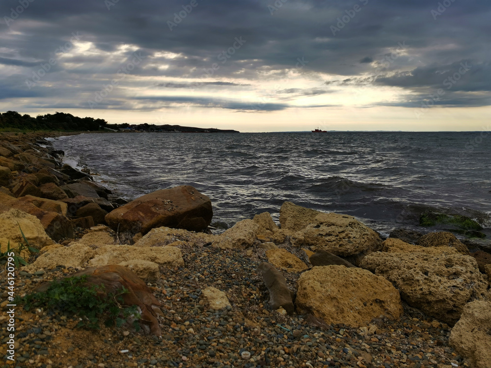 Dark storm clouds over the Sea of Azov. Taman, Krasnodar Territory, Russia. Stones, waves, low dark clouds. The silhouette of a ship on the horizon