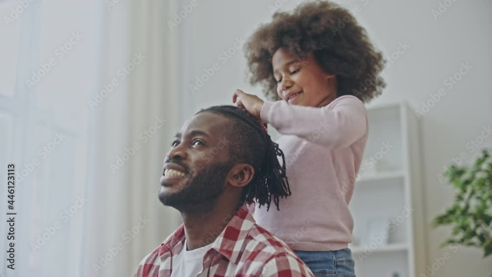 Little african girl doing hairstyle for happy dad, family spending time together