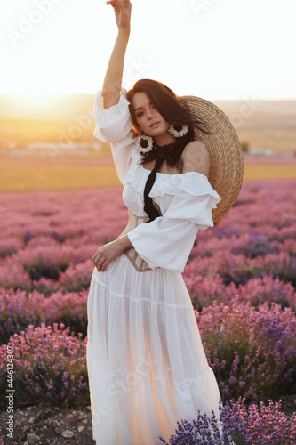 beautiful woman with dark hair in elegant white dress posing in bloomig lavender field on sunset photo