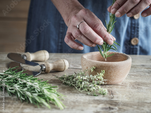 Female hands and fresh organic rosemary on vintage wooden table. Copy space.