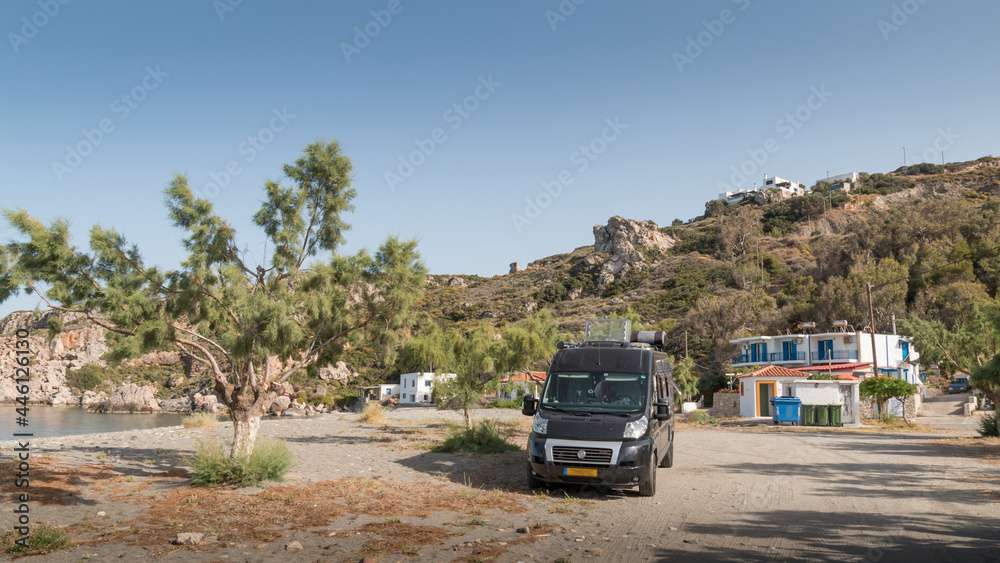 Black campingcar wildcamping at a desolated small beach with some houses in the background on the island of Kythira, Greece