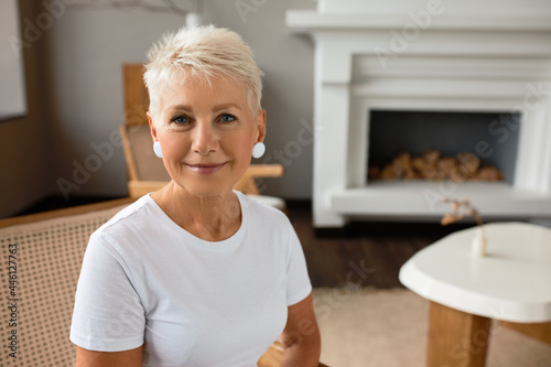 Mature lady sit in new apartment after fresh renovation. Middle aged woman enjoy interior design and quality of work. Cozy sitting room with fireplace and coffee table. Interior concept. Copy space