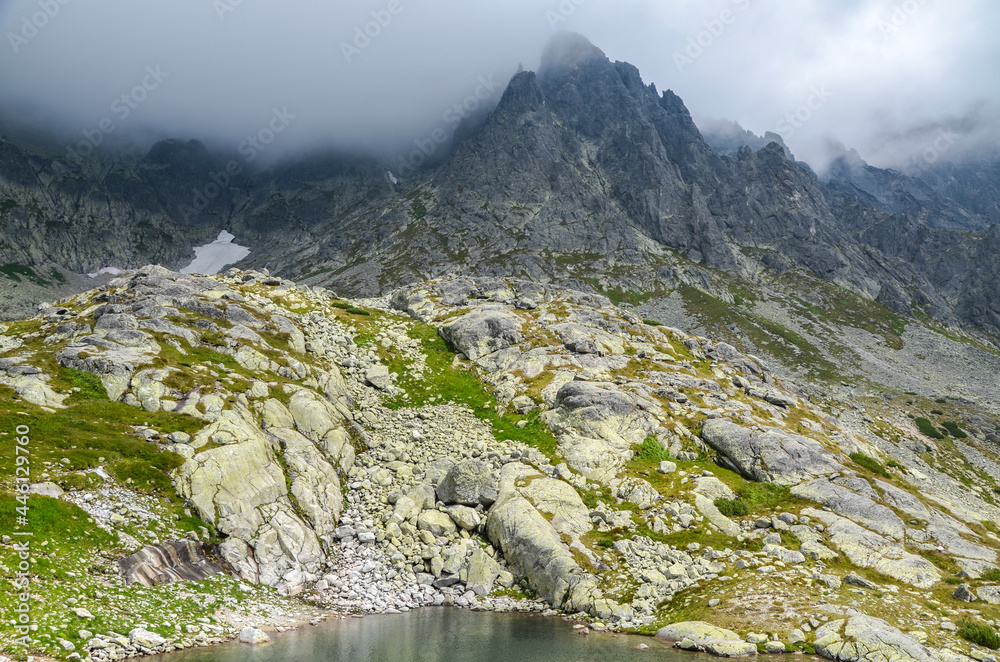 Obraz premium Jagged and sharp ridges rock emerge from the mist above and rain clouds at High Tatras National Park, Slovakia