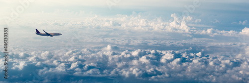 Passenger airplane over clouds on panoramic sky background with copy space. Wide landscape with aircraft for your concept of the air trip, journey or international air transportation.