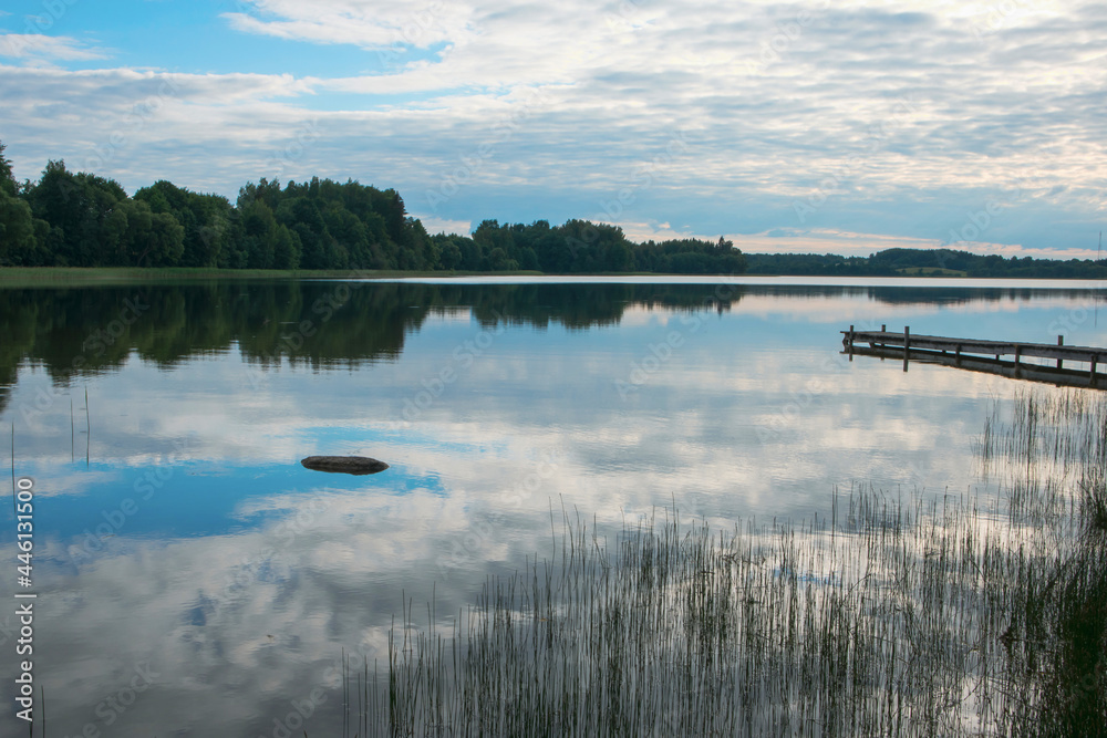 A quiet lake with a reflection of clouds and an old wooden footbridge A quiet lake with a reflection of clouds and an old wooden footbridge