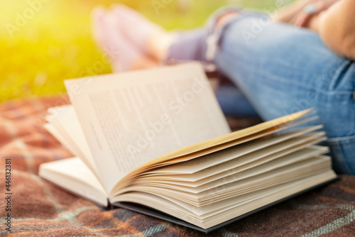 A woman in jeans with a book and a cup of coffee sits on a blanket in the park